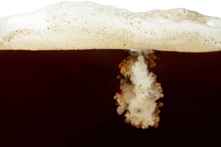 Closeup process of making latte, cappuccino, pouring milk, cream into transparent glass cup of coffee with foam. Abstract brown background with light stains. Mixing of liquids. Hot caffeine drinks. の写真素材