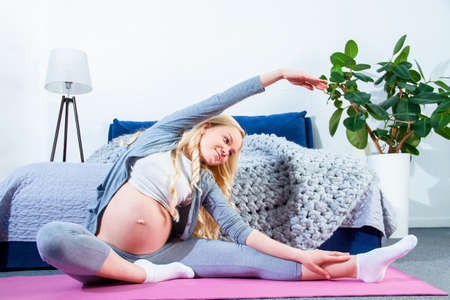 Young pregnant woman is doing exercises, gymnastics, fitness at home. Girl is preparing for childbirth, keeping fit during pregnancy, gestation. Expectation of baby concept. Healthy lifestyle.の写真素材