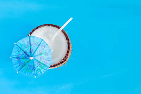 Brown half of coconut nut with white milk and straw inside on blue background. Tropical exotic fruit, cocktail, water for refreshment. Organic natural healthy vegan meal, coco based food concept.の写真素材