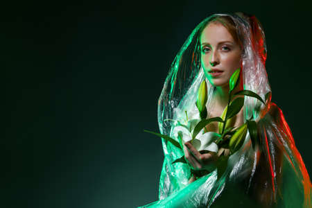 Portrait of girl, holding white flowers symbol of green nature. Young woman wrapped, covered in plastic bags, polyethylene. Earth is suffering from ecological environmental pollution problems.の写真素材