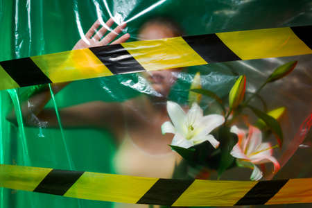 Portrait of girl, can no breathe, holding white flowers. Young woman is choking, wrapped in plastic...