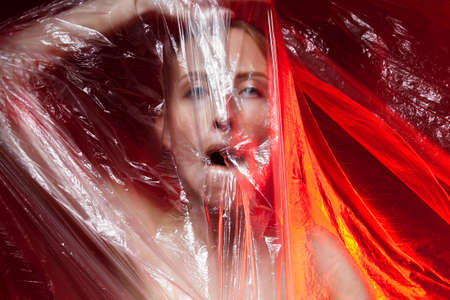 Portrait of dying unhappy girl, can no breathe. Young woman is choking, wrapped in plastic bags,...