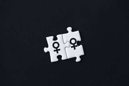 Two pieces of puzzles with printed female venus signs are stacked together on black background. Concept of equality, acceptance of sexual minorities lesbian, gay, bisexual, transgender in society.の写真素材
