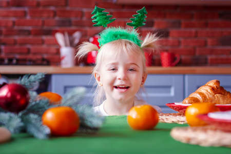 Adorable girl holding with green Christmas tree hat. Little child in festive clothes decorating Christmas tree with family. Girl playing and smiling during celebrating Christmas eve eveningの写真素材