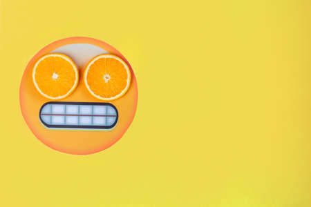Slices of citruses are laid out like glasses on eyes of funny emoji sign icon in left side of background. Pieces of orange are lying on paper emoticon on yellow canvas. Summer mood concept.の写真素材