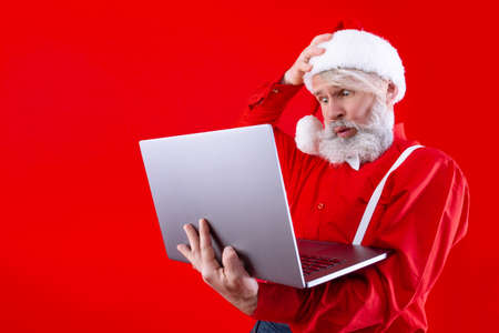 Serious modern Santa Claus, wearing stylish red hat, shirt and suspenders. Shocked, old man with...