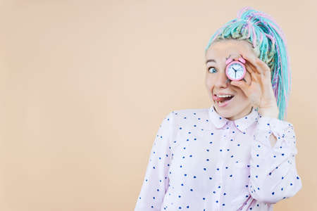 Surprised girl freelancer is holding pink alarm clock. Young woman with colored dreadlocks is shocked, worried about overdue. Stress, deadline concept. Problems due to delays terms. Emotional portraitの写真素材