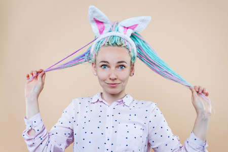 Pretty cute girl in bunny ears, pink shirt is smiling. Young woman with colored dreadlocks is...