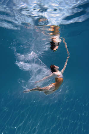 Fashionable and athletic girl free diver alone in the depths of the ocean. Swimmer brunette diving...