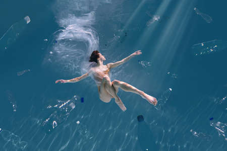 Fashionable and athletic girl free diver alone in the depths of the ocean. Swimmer brunette diving deep in ocean on blue underwater background. Pollution, plastic and ecology conceptの写真素材