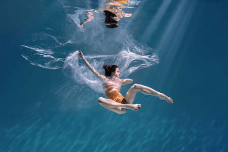 Fashionable and athletic girl free diver alone in the depths of the ocean. Swimmer brunette diving deep in ocean on blue underwater background. Pollution, plastic and ecology conceptの写真素材