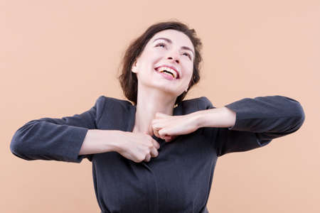 Young business woman wearing casual jacket standing over isolated beige background, doing positive gesture with hands, smiling and happy. Cheerful expression and winner gesture. Happiness conceptの写真素材