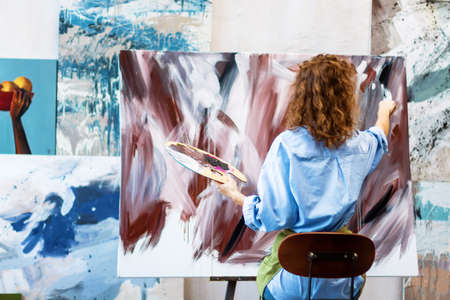 Back view woman artist is drawing abstract picture in workshop studio gallery. Process of creating...