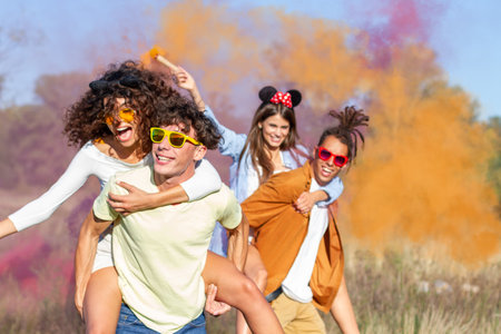 Beautiful young man and woman hold light up colored smoke bombs - Happy friends having fun in the park with multicolored smoke bombs - Young students celebrating spring break together. Holi festival.の写真素材