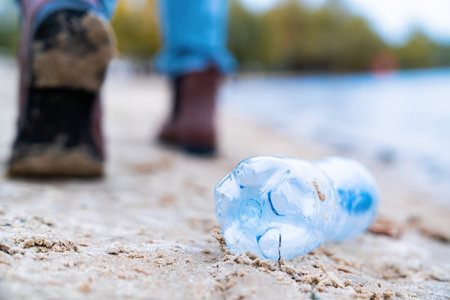 Closeup garbage plastic bottle thrown by female on city beach. Trash on nature. Environmental...