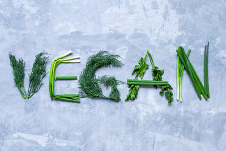 Inscription text vegan laid out from natural juicy healthy greens on gray concrete background. Urban vegetable garden concept. Eco ecological organic food. Autumn harvest. Farming and agriculture.の写真素材