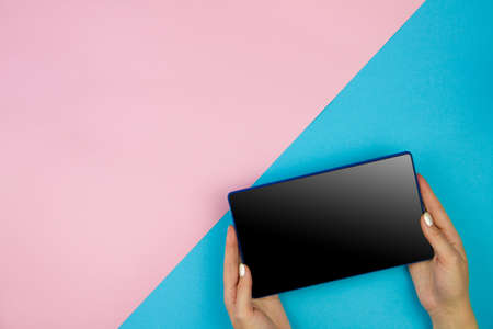 Young woman hand holding tablet with black screen on light pink blue table background. Copy space empty place for text inscription. Mobile application interface concept design. Modern technology.の写真素材