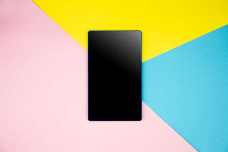 Mockup black blank tablet screen display on yellow, blue, pink background. Flat lay, top view. Copy space for advertising text inscription. Modern technology, web application for gadgets concept.の写真素材