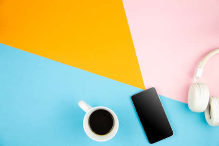 Blue orange pink desk office with smartphone, cup of coffee, white headphones. Top view with copy space for input text inscription. Designer workspace on table essential elements on flat lay.の写真素材