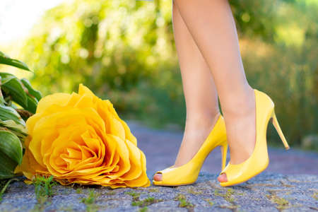 Girl young woman in yellow high heel shoes is walking from side to side in park, forest, along path with green plants leaves. Closeup beautiful slender female legs. Holiday weekend, wedding concept.の写真素材