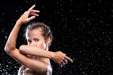 Portrait of sports woman doing stretching under drops of rain. Girl dancer is dancing. Drops of water fall on face against black background. Freedom, freshness concept. Modern art and beauty.の写真素材