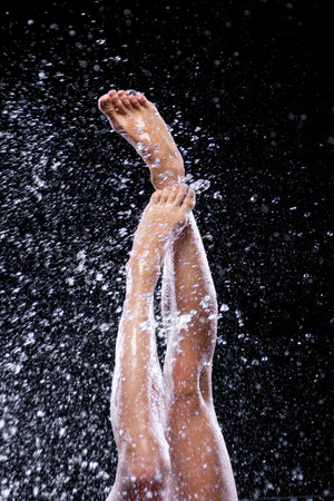 Closeup athletic wet modern ballet dancer legs under splashes, streams, drops of rain water. Woman girl is dancing, doing acrobatic tricks. Contemporary art dance. Freedom and freshness concept.の写真素材