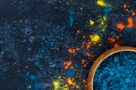 Top view of bright traditional holi paints in wooden bowls isolated on dark background. Colorful...