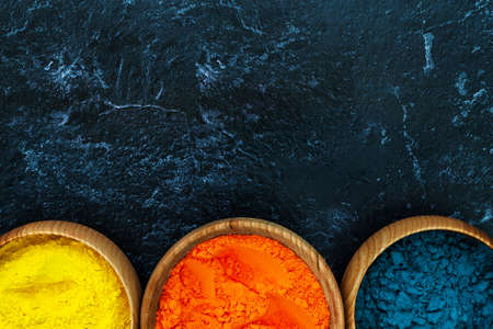 Top view of colorful bright traditional holi paint powder in wooden bowls isolated on dark concrete background. Copy space for text. Happy holiday. Concept of Indian color festival called Holi.の写真素材