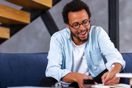 Skilled african man freelancer sit in comfortable pose work from home consult client by video link write programme code on pc. Young black guy relax at home with laptop post comments at social networkの写真素材