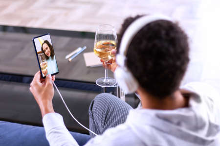 African american man is holding smartphone, chatting online with friend, sitting at home. Black guy is talking with girlfriend by video conference. Wireless technology. Communication during quarantineの写真素材