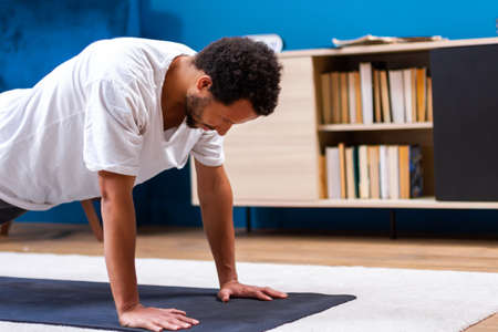 Young  African American is holding his body in yoga position, getting active while isolated during...