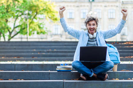 Portrait of happy emotional student passed exam at university. Young man is studying with laptop...