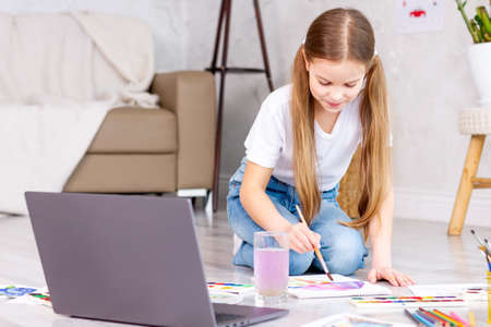 Remote school art lessons. Child smiles studies and gets knowledge remotely. Little girl study online at home does homework. Distance learning education. Quarantine and Social distancing concept.の写真素材
