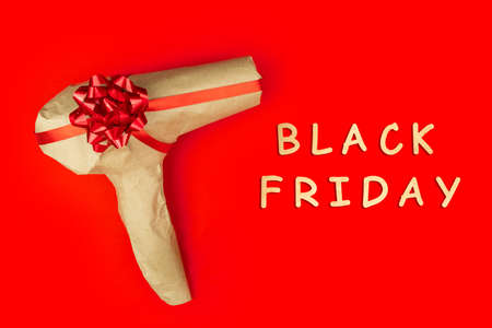 Eco rustic beige recycled Christmas new year gift, hand hold hair dryer wrapped in craft paper with red ribbon on red color background. Holiday present Care package. Black Friday Cyber Monday conceptの写真素材