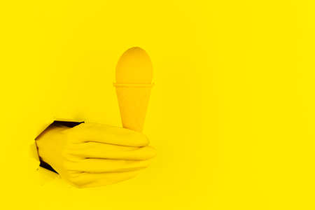 Abstract yellow background with female hand in latex gloves is holding egg in colorful ice cream cone. Minimal art design. Minimalist meal, fashion style. Festive food court. Happy Easter festival concept.の写真素材