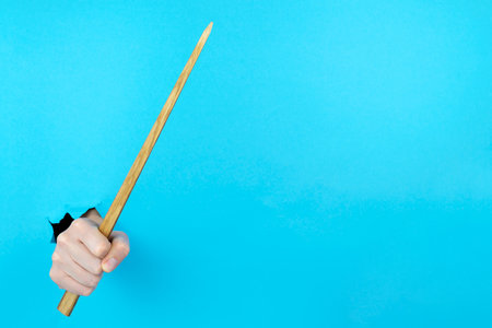 Female hand is holding wooden teacher pointer in torn hole of blue background. Back to school concept. Education at university, college. Copy space for text. Mockup, template for 
lecture schedule.の写真素材