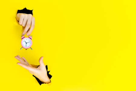 Ringing twin bell vintage classic pink alarm clock in female hand isolated in torn hole of yellow...