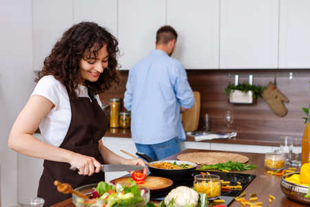 Overjoyed millennial man and woman have fun cooking healthy tasty vegetarian salad in kitchen...
