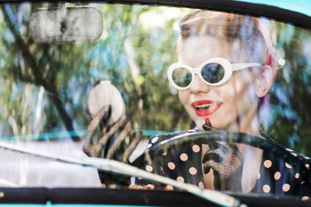 Beautiful stylish woman in vintage bright dotted clothes, sitting in mint old car. Fashion pin-up...