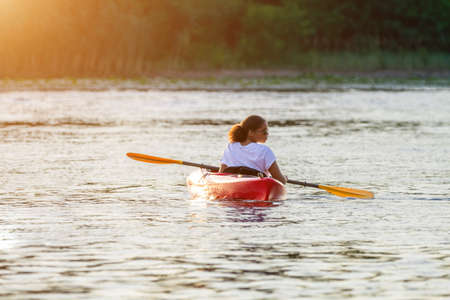 Confident young woman kayaking on river alone with sunset in the backgrounds. Having fun in leisure activity. HÑalthy active girl spend weekend outdoors on the kayak boat. Sport, relations conceptの写真素材