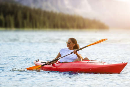 Confident young woman kayaking on river alone with mountains sunset in the backgrounds. Having fun in leisure activity. HÑalthy active girl spend weekend on the kayak boat. Sport, relations conceptの写真素材