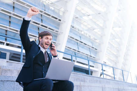 Portrait of young stylish tide up businessman in formal suit use  mobile phone and laptop, smiles...