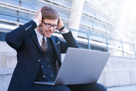 Portrait of stressed businessman with his head in hands frustration. Trying to concentrate. Overworked manger in big city business district. Upset man wearing suit sitting in front of his laptopの写真素材