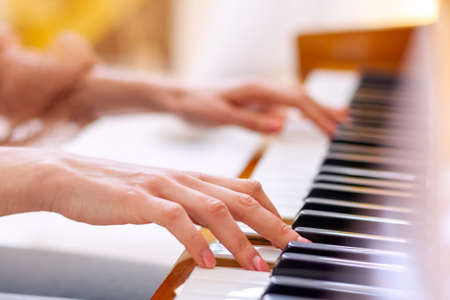 Close up of hands young talented woman playing the piano at home, performing classical music, getting ready to the classes in the music school. Musical artist create instrumental acoustic melody.の写真素材