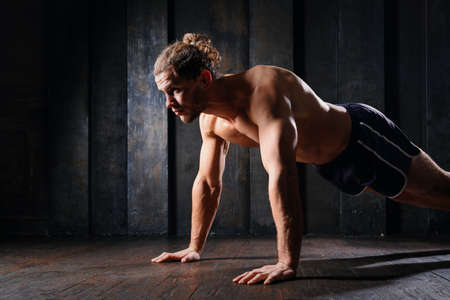 Young athletic guy in blue shorts on floor doing plank exercise on floor. Active strong fit...