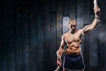 Strong muscular bodybuilder man with heavy rope in hands and perfect body after training. Athlete do exercise fitness with ropes. Male training upper body working out at hard cross-fit training.の写真素材