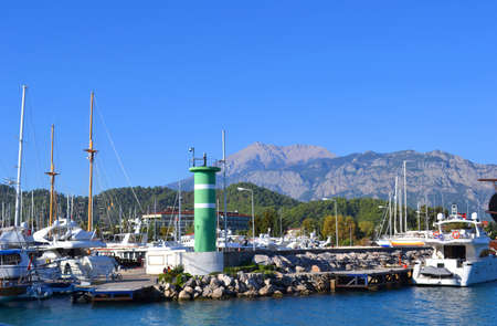 Berth for yachts, ships and boats with a lighthouse on the background of mountainsの写真素材
