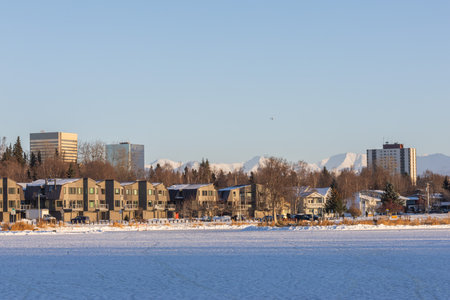 Anchorage Residential District with Downtown Skyline. Peaceful suburban scene in Anchorage, Alaska, showing houses, trees, snow, and the urban skyline set against mountain peaks.の写真素材