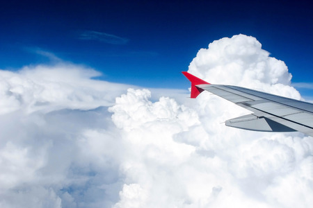 Red wing of airplane flying above the clouds.の写真素材