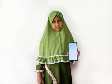 Indonesian Muslim girl holding a smartphone in front of a white background, wearing green clothes